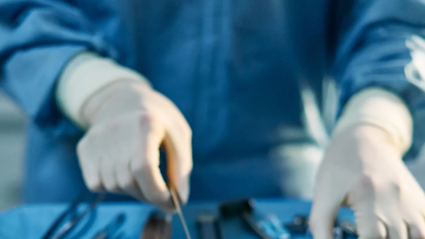 Manos de un cirujano con guantes que ordenan instrumentos quirúrgicos sobre una mesa cubierta en un quirófano, antes de una abdominoplastia