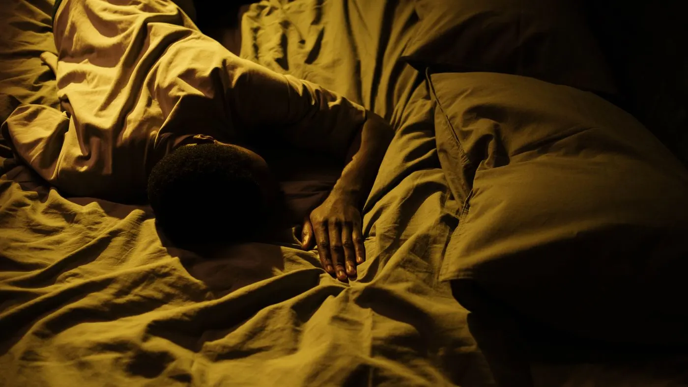 Persona dormida de lado sobre sábanas arrugadas, en un cuarto a oscuras con luz ámbar: la hora de la noche en que se notan los ronquidos y las pausas al respirar de la apnea del sueño