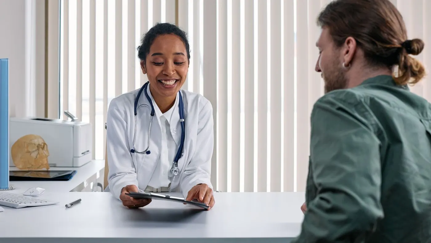 Doctora con bata blanca y estetoscopio que muestra una tableta a un paciente sentado frente a ella en un consultorio, como en la valoración previa a un bypass gástrico