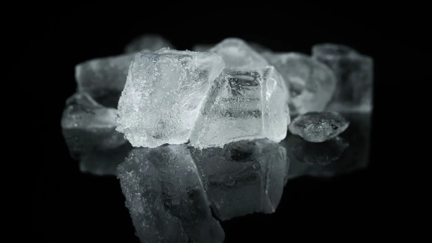 Cubos de hielo transparentes con su reflejo sobre una superficie negra, imagen del frío controlado que se aplica sobre la grasa en la criolipólisis