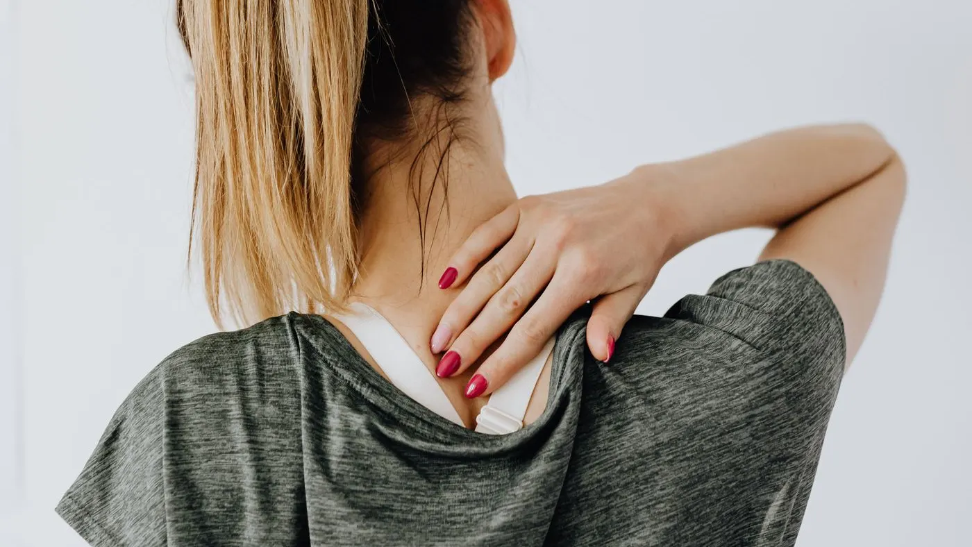 Mujer vista de espaldas, con el pelo recogido, que se lleva la mano a la parte de atrás del cuello; el cuello es la zona donde está la glándula tiroides
